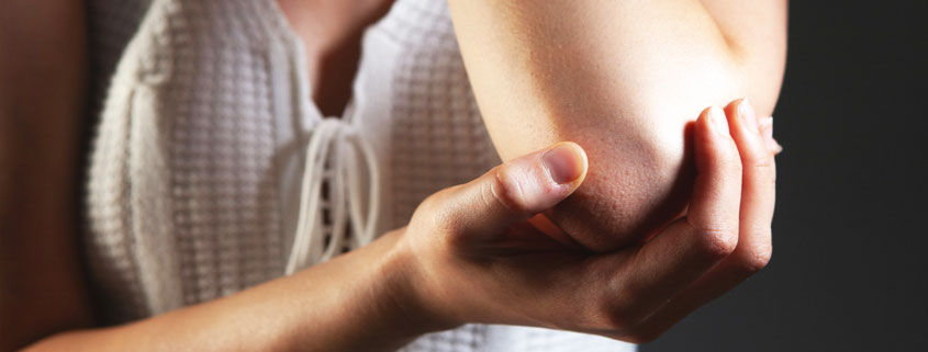 Close-up of a young woman holding her elbow while experiencing joint pain and discomfort